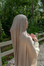 Person wearing a beige hijab in a forest setting